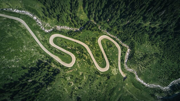 An overhead photo of a winding road amongst green hills.