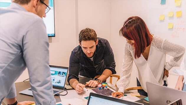 The Resolution Digital team work on a project together, writing on paper and using their laptops.